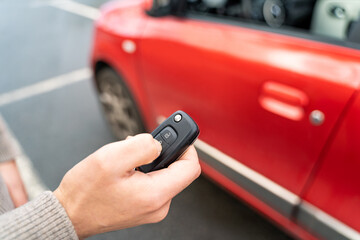 Male hand of young man holding electronic remote key pushing button near red rental car to open or close it. Travel, tour, tourism, journey, mode of transport, technology, ecology, car sharing.