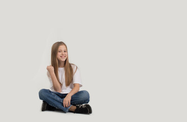 a beautiful teenage girl in a white T-shirt and blue jeans is sitting on a white background