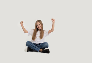 a beautiful teenage girl in a white T-shirt and blue jeans is sitting on a white background