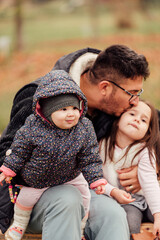 Fototapeta premium A single father with two daughters sitting on a bench in the park