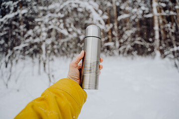 Hold a gray thermos with tea in your hand. Metal thermos of silver color. Made of steel.