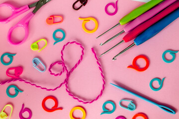 Bright crochet tools on a pink background. Crochet hooks, colored markers, needle and scissors.