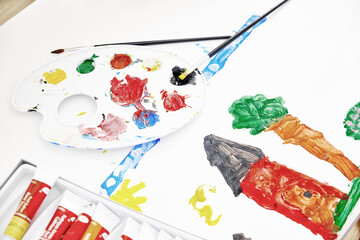 Palette with mixed paints, paintbrush and painting of little girl. High angle view. Painting shows...