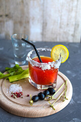 Bloody Mary - a cocktail containing vodka, tomato juice, various celery spices with black olives on skewers decorated with lemon on a wooden board