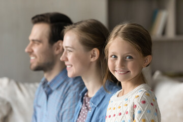 Head shot smiling adorable preteen small child girl looking at camera while happy young couple parents looking in distance, friendly two generations family heredity, dynasty, union, relations concept.