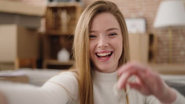 Young blonde woman having video call holding key of house at new home
