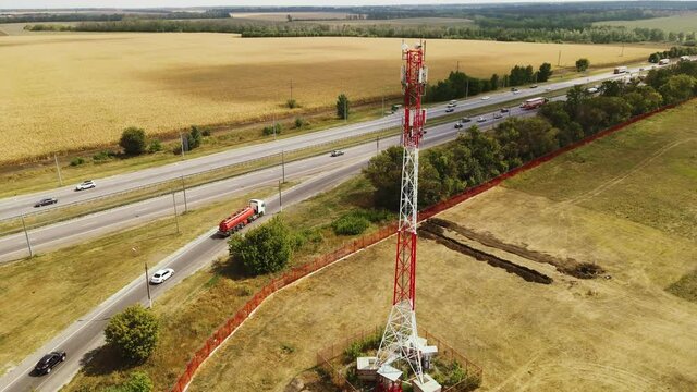 Telecommunication Antenna receiver on cell phone tower with 5G base station transceiver near highway with car traffic, aerial view.