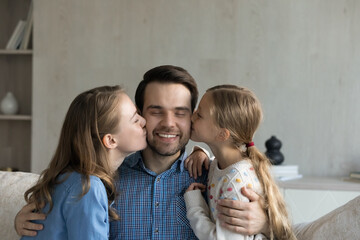 Happy affectionate young mother and small preteen kid daughter kissing cheek of smiling handsome father, showing loving candid feelings at home, expressing devotion, sincere relations concept.