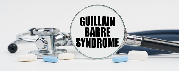 On a white surface are pills, a stethoscope and a magnifying glass inside which is written - guillain barre syndrome