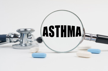 On a white surface lie pills, a stethoscope and a magnifying glass with the inscription - ASTHMA