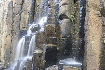 naturally formed basalt prisms have water coming from a stream that falls like a waterfall

