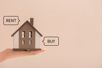 Female hand with figure of house on beige background. Concept of choice between renting and buying