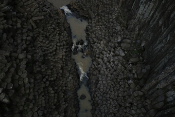 naturally formed basalt prisms have water coming from a stream that falls like a waterfall

