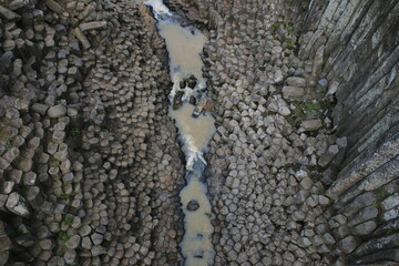 naturally formed basalt prisms have water coming from a stream that falls like a waterfall

