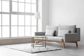 Comfy grey sofa with table and lamp near light wall