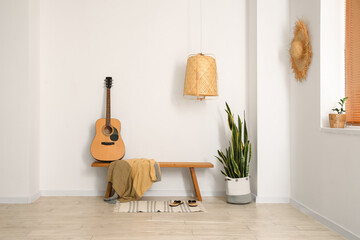 Interior of light room with wooden bench, guitar and houseplant