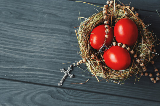 Easter background with dark red Easter eggs in nest and catholic rosary with a cross. Top view with copy space