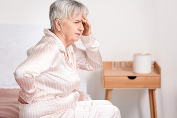 Senior woman suffering from back pain on bed at home