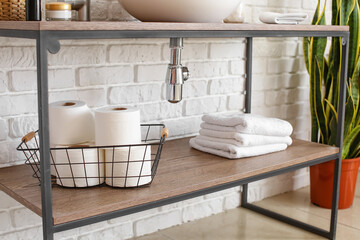 Basket with toilet paper rolls on shelf near white brick wall