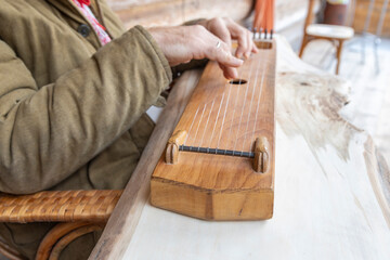 A man in ethnic clothes plays an ancient musical instrument. A man in a brown linen quilted jacket...