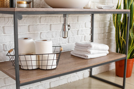 Basket With Toilet Paper Rolls On Shelf Near White Brick Wall