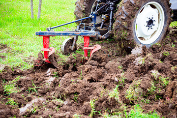 The tractor plows the land in the garden with a plow in early spring. Preparing the soil for...