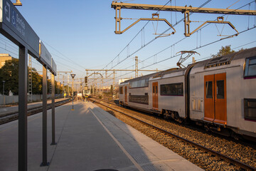 Naklejka premium Rail travel. Modern intercity train on a railway platform. Passenger train on the railway in the evening. Railway station Castelldefels. Platform, rails and wires going into perspective.