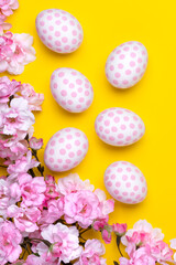 Easter background with polka dot paschal eggs, flat lay with cherry blossom tree branches. Spring season. Minimal design, festive floral greeting card. Yellow backdrop.