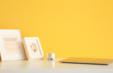 Pictures, portable speaker and modern laptop on table near color wall