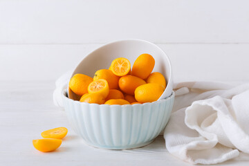 Bowl with tasty kumquat fruits on light wooden background