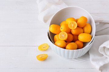 Bowl with tasty kumquat fruits on light wooden background