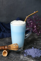 Cup of blue matcha latte, powder and chasen on dark background