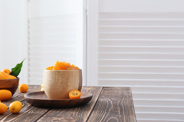 Bowl of tasty kumquat jam and fresh fruits on table