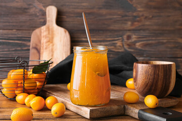 Jar of tasty kumquat jam and fresh fruits on wooden background