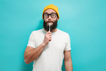 Portrait of handsome man with beard wearing glasses enjoying delicious meal with fork in studio...