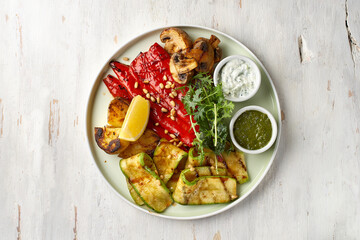 Grilled vegetables eggplant, zucchini, pepper salad with tzadziki Greek yogurt sauce on a light background, top view. Delicious appetizer, tapas, snack