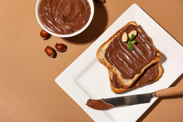 Plate of bread with chocolate paste and hazelnuts on beige background