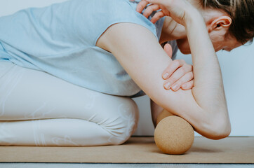 Side view of person doing myofascial release on triceps muscle with a large cork ball on cork yoga...