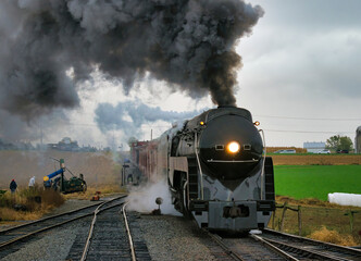 Naklejka premium An Antique Restored Steam Freight Train Approaching Head on Blowing Smoke and Steam