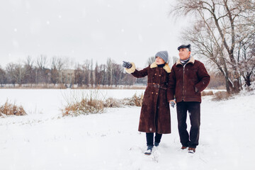 Senior family couple walking outdoors during snowy winter weather. Elderly people holding hands....