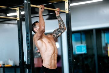 Portrait of shirtless man doing pull-ups at gym