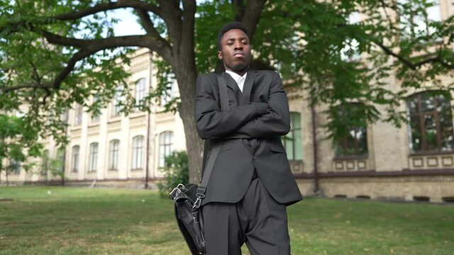 Portrait of elegant confident man crossing hands looking at camera with serious facial expression. Smart stylish African American teacher student standing at university campus outdoors posing