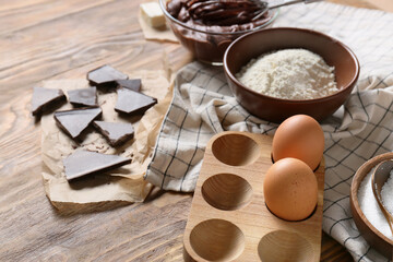 Holder with eggs and ingredients for preparing chocolate brownie on wooden background