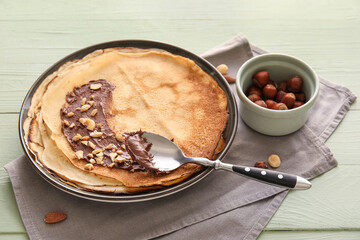 Plate of tasty thin pancakes with chocolate paste and nuts on green wooden background