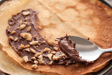 Tasty thin pancakes with chocolate paste and nuts on plate, closeup
