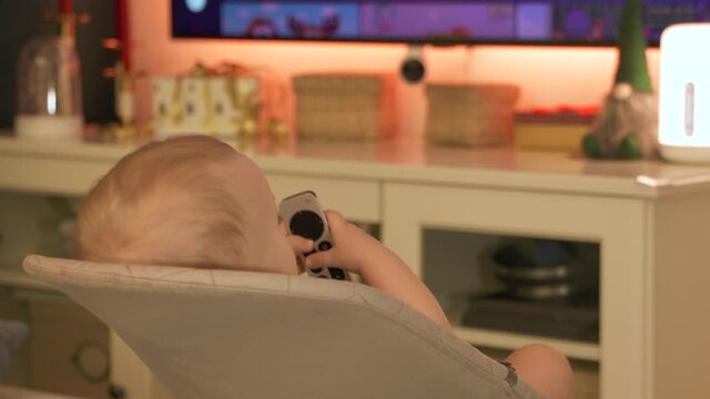 Caucasian small baby watching TV at home, cute little toddler child holding remote control for TV digital media player. High quality 4k footage
