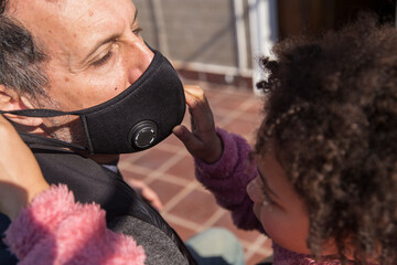 Cute little mixed race girl is helping with love her european father with a protective mask in a wheelchair after recovering from covid19 variant omicron outdoor.