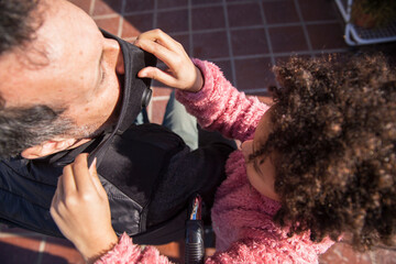 Cute little mixed race girl is helping with love her latin father with a protective mask in a...