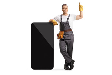 Full length portrait of a repairman in a uniform leaning on a big smartphone and pointing up