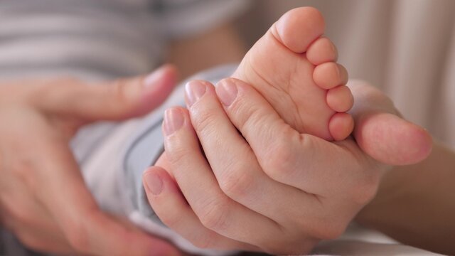 Children's feet, mother's hands massage. Happy family concept. Children's legs, mother hugs the baby with her hands. Happy mother, child play together. Baby care. Childhood, family moments